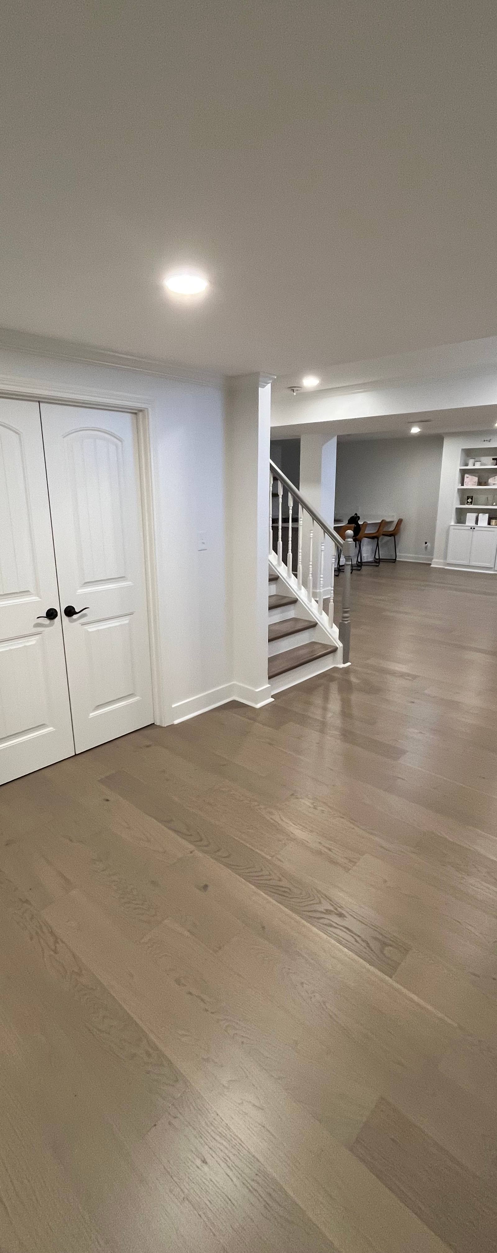 Open layout finished basement with custom entertainment center, white spindle staircase, and wide plank hardwood flooring