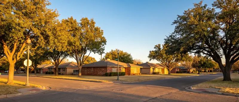Quiet Lubbock residential street with brick ranch homes and mature trees at golden hour