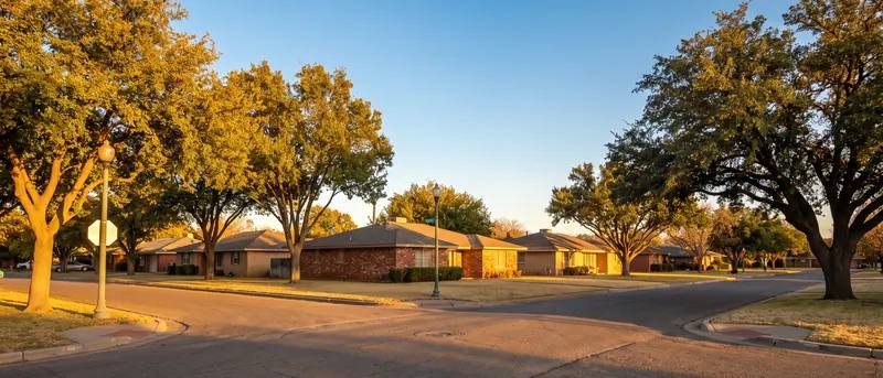 Quiet Lubbock residential street with brick ranch homes and mature trees at golden hour