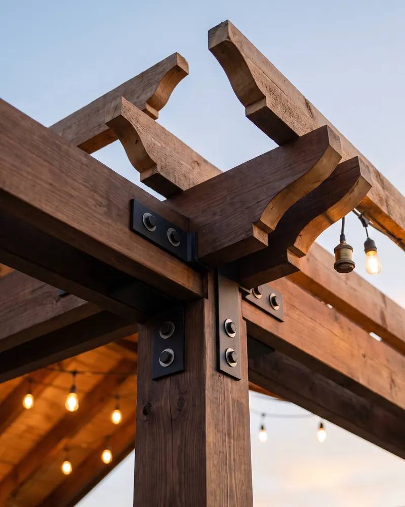 Looking up at the joint where a dark stained timber post meets a beam, with black steel brackets and rafter tails