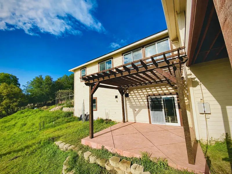 Stained timber pergola over a patio behind a two-story home