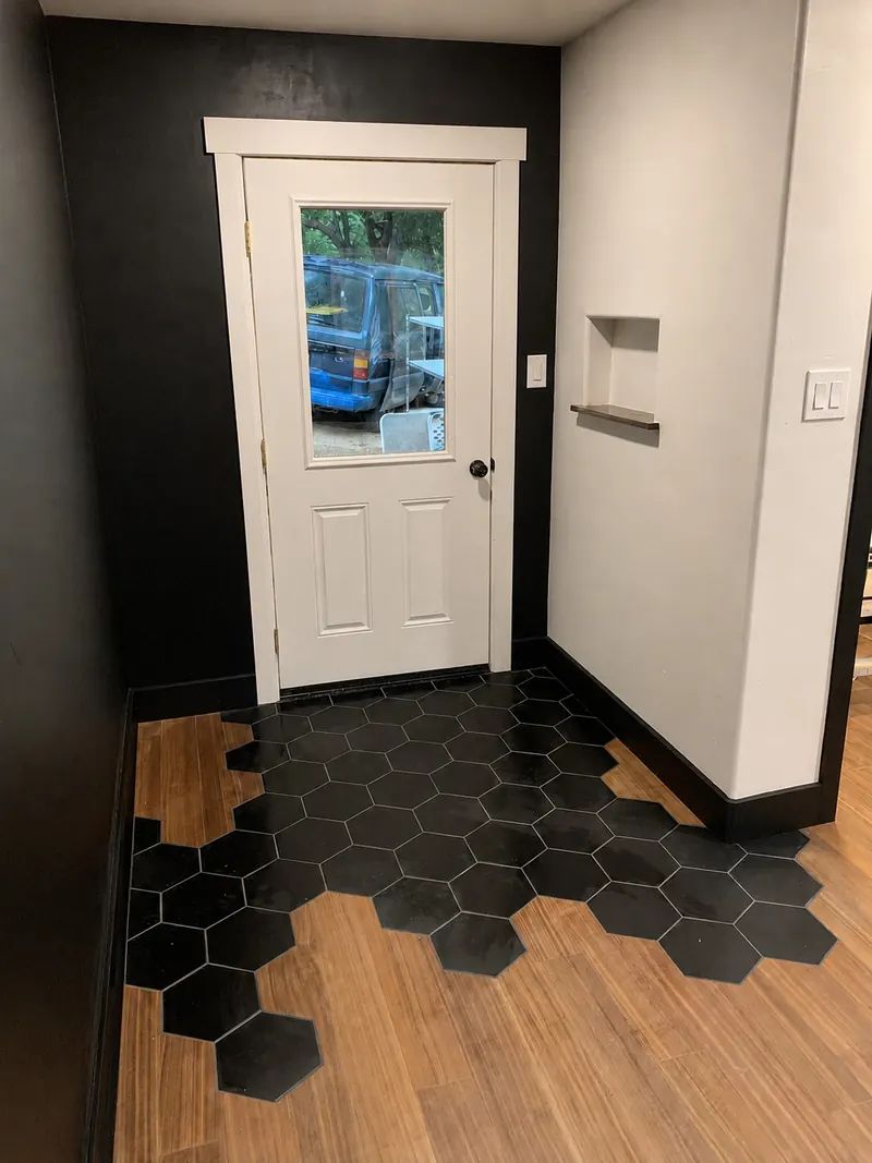 Entryway where black hexagon tile is inlaid into walnut flooring