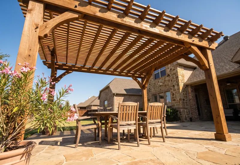 Freestanding cedar pergola with knee braces over a dining table on a paver patio in bright late morning sun