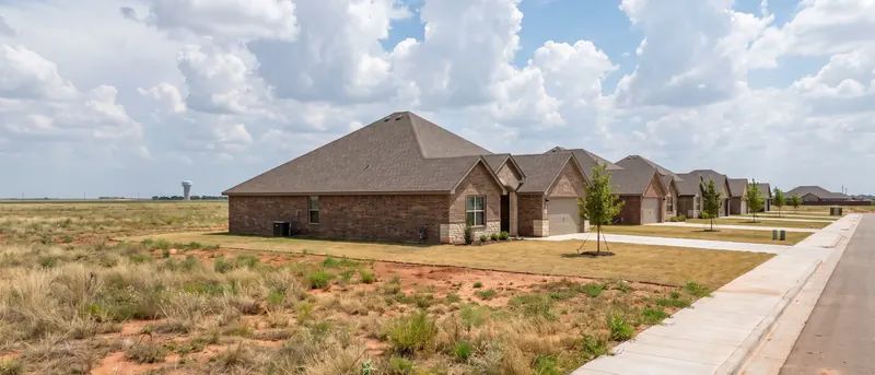 New houses beside open plains at the edge of Shallowater under tall afternoon clouds