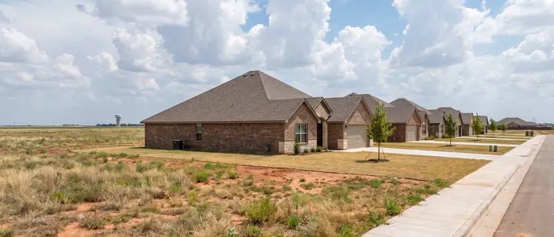 New houses beside open plains at the edge of Shallowater under tall afternoon clouds