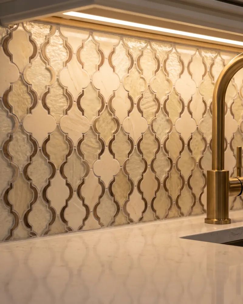 Close view of a glass and stone mosaic backsplash meeting a quartz counter under cabinet lighting