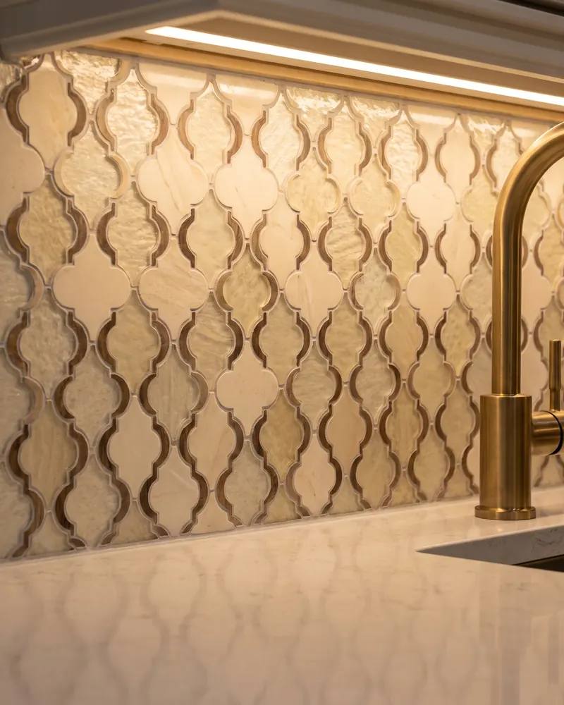 Close view of a glass and stone mosaic backsplash meeting a quartz counter under cabinet lighting
