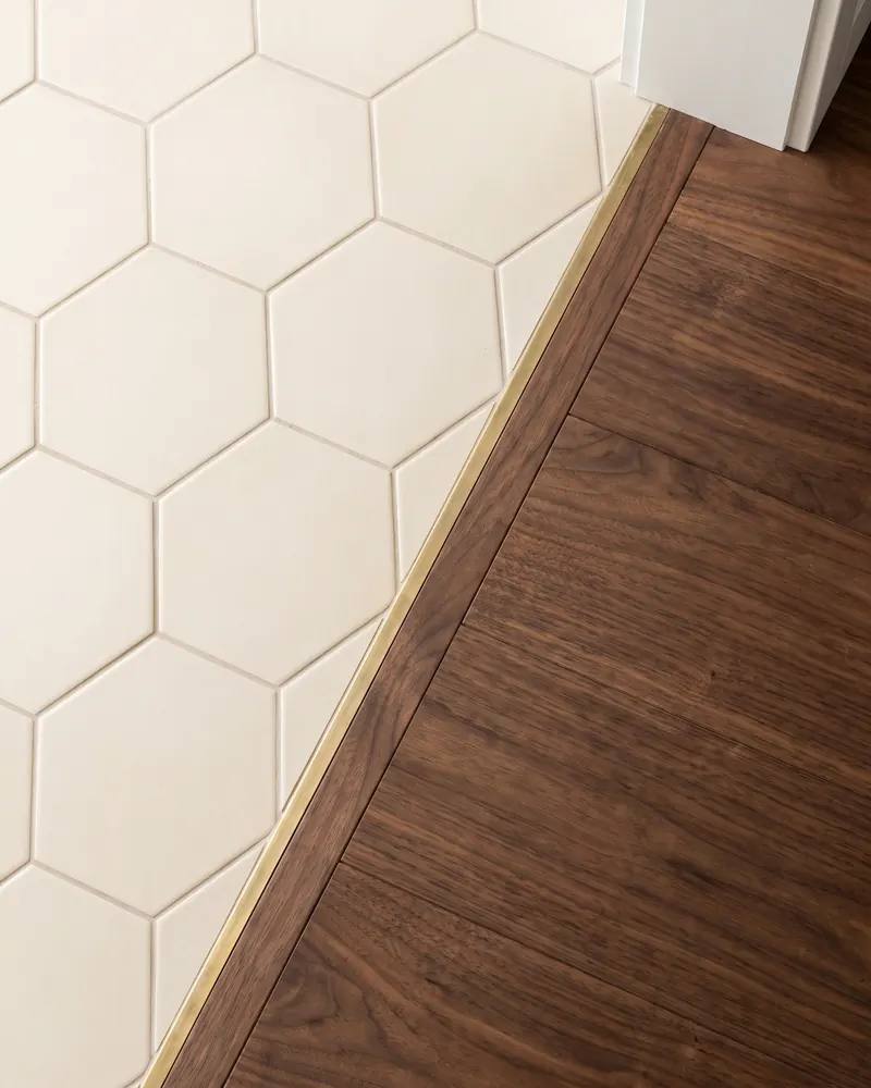 Overhead view of an entry where hex tile meets walnut flooring along a fitted inlaid border