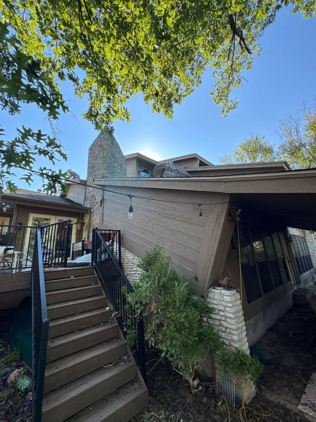 Wood siding and deck stairs near a stone chimney ahead of a repaint in Austin, TX by Hill Country Painting
