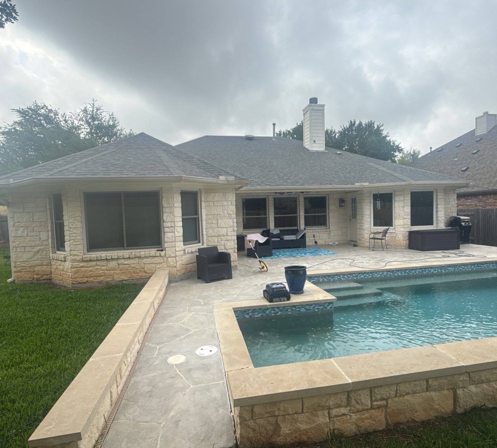 Back elevation of a stone home with pool ahead of exterior painting in Cedar Park, TX by Hill Country Painting