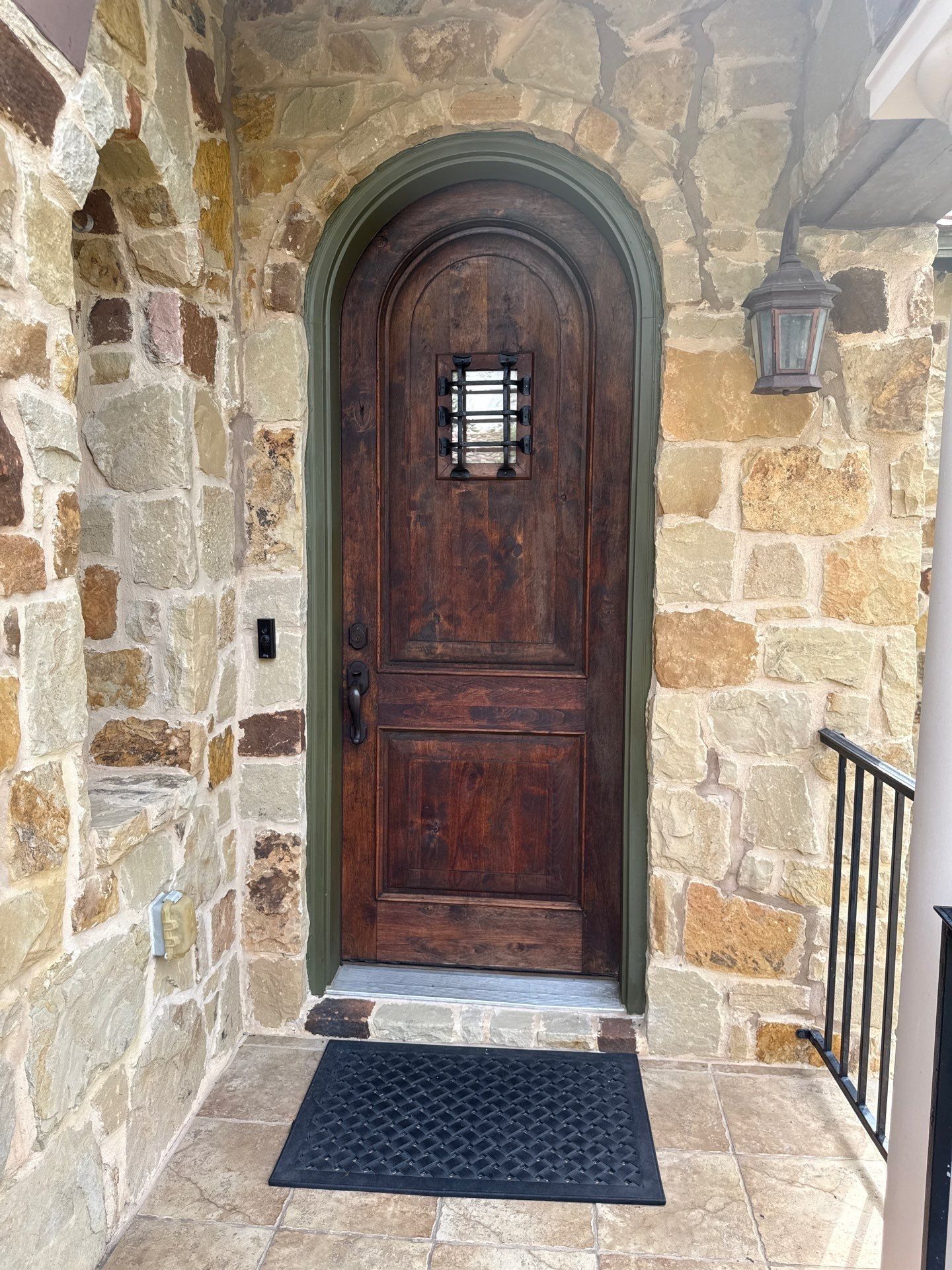 Arched wood front door with stone surround on a home in Austin, TX ahead of exterior painting by Hill Country Painting