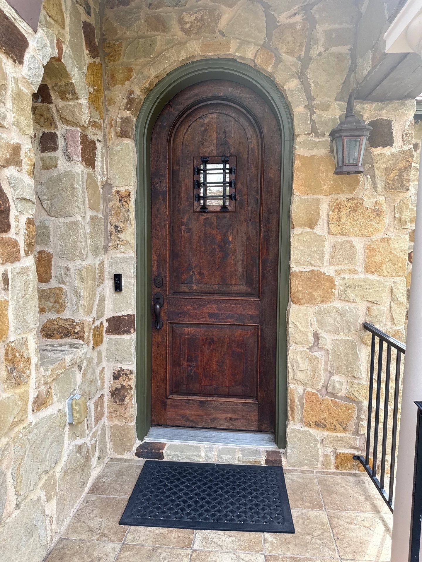 Arched wood front door with stone surround on a home in Austin, TX ahead of exterior painting by Hill Country Painting