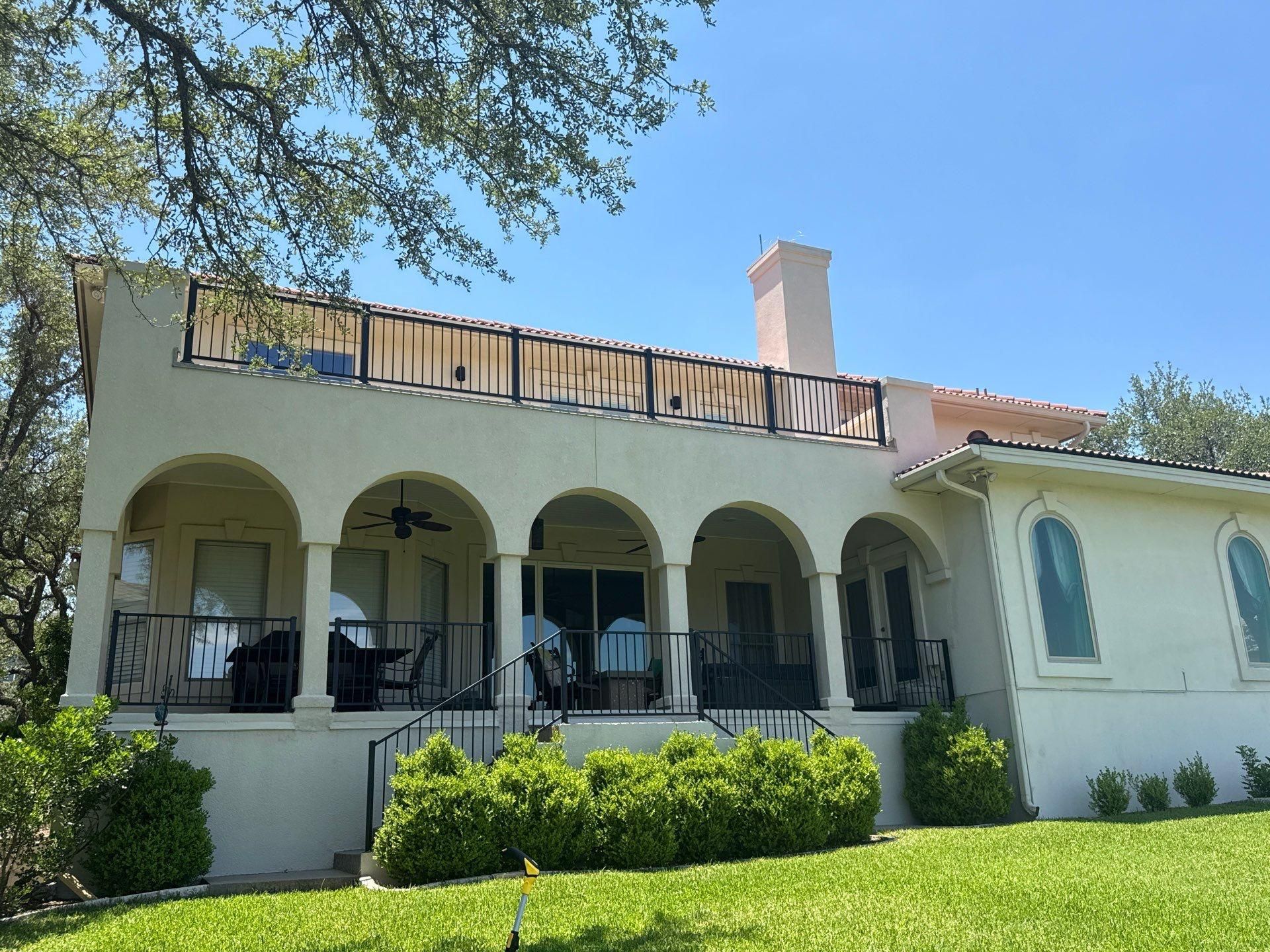 Back exterior with arched covered porch and second-story balcony of a home in Lakeway, TX ahead of exterior painting by Hill Country Painting