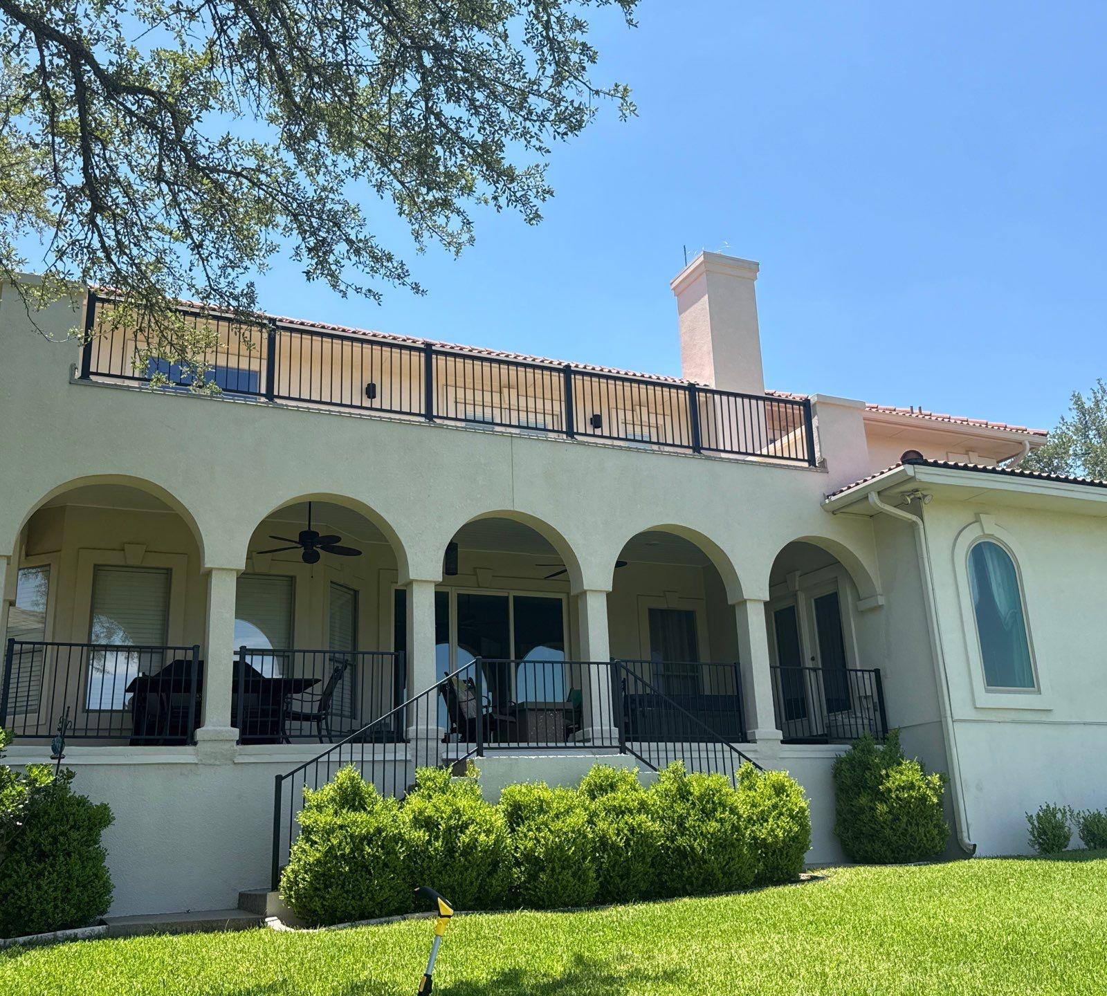 Back exterior with arched covered porch and second-story balcony of a home in Lakeway, TX ahead of exterior painting by Hill Country Painting