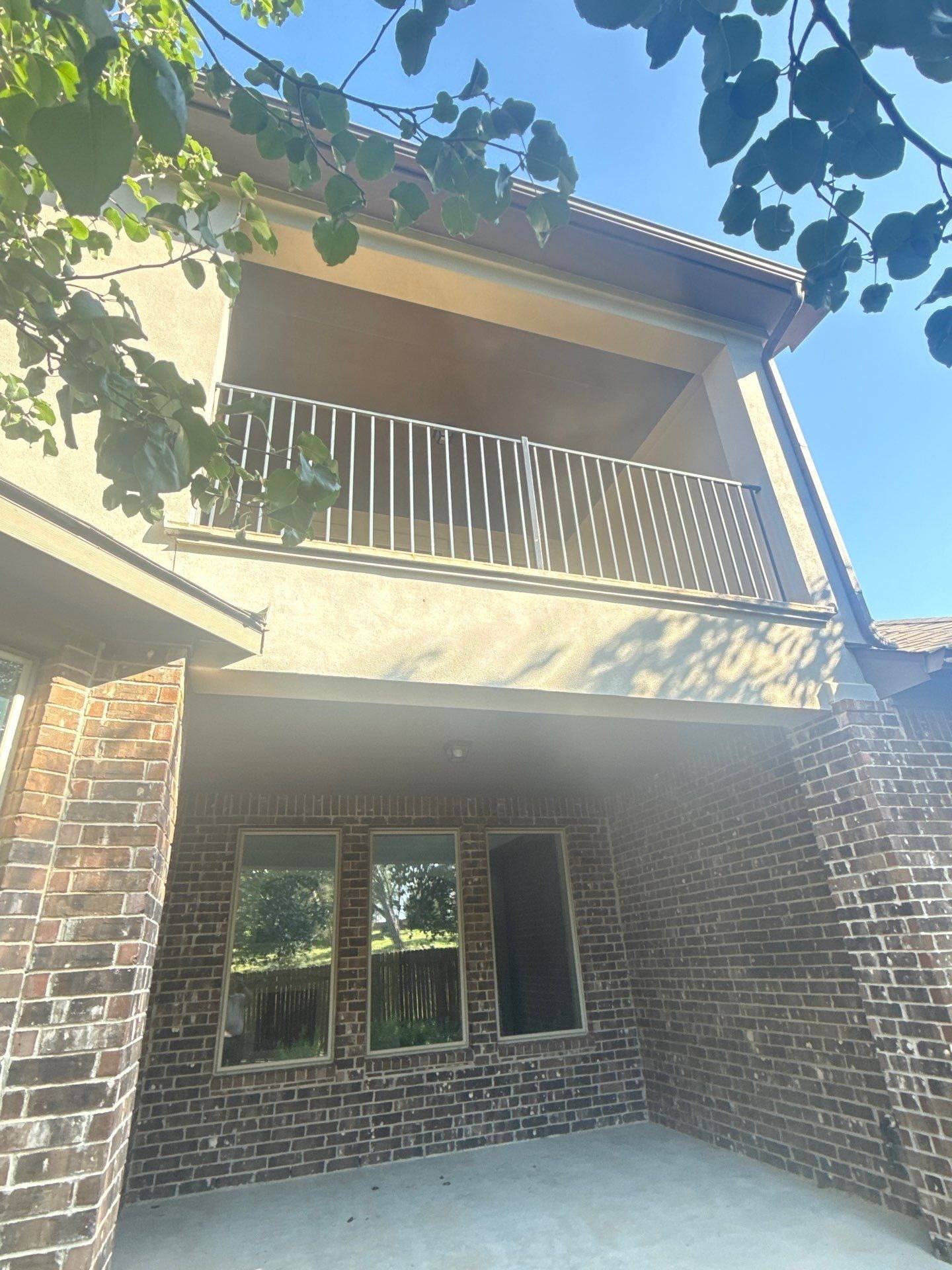 Back exterior with covered patio and balcony at a home on Borho Ranch St in Leander, TX prepared for a painting estimate by Hill Country Painting