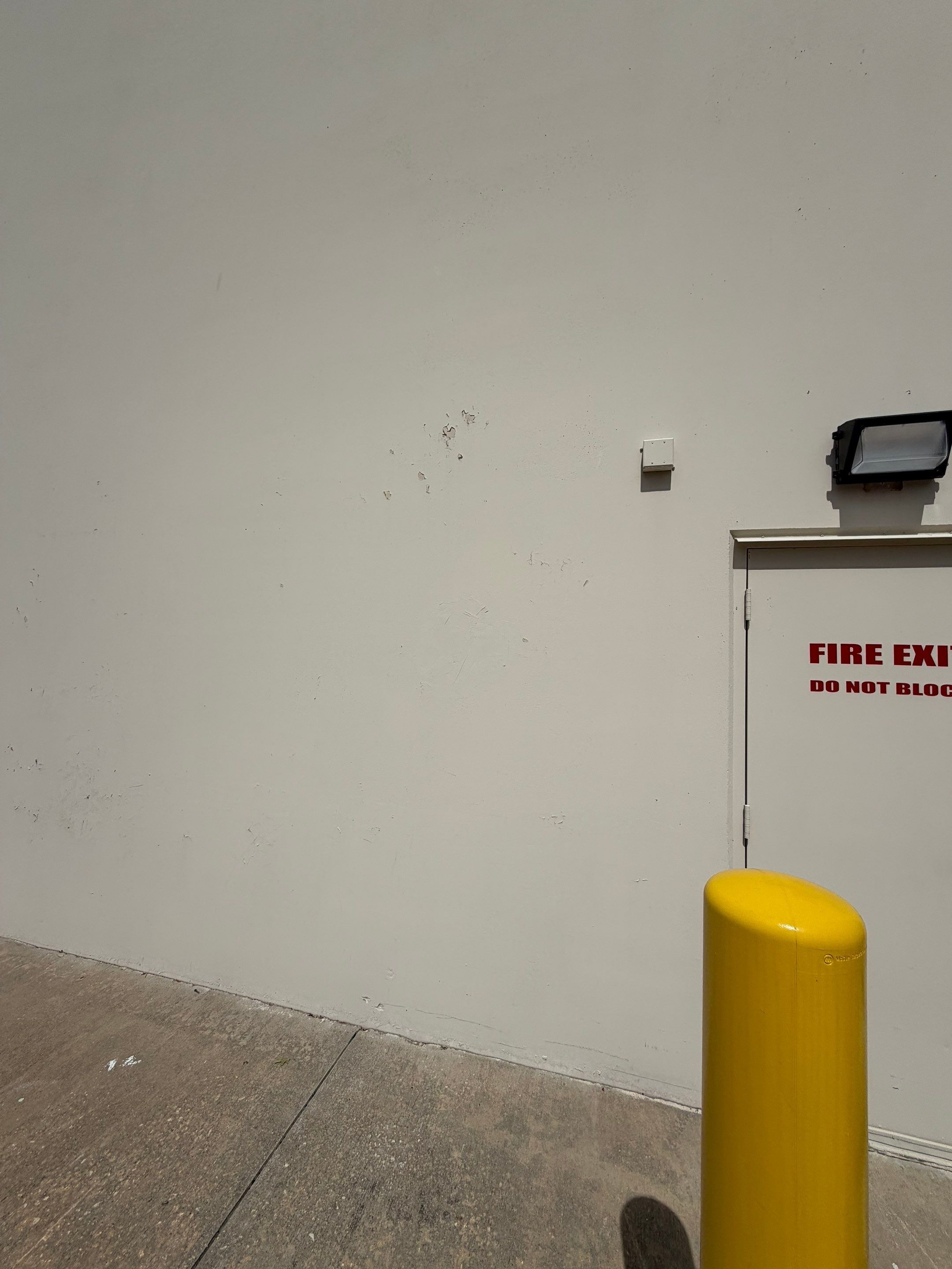Exterior wall near a fire exit door of a commercial building on Highway 79 in Hutto, TX ahead of exterior painting by Hill Country Painting