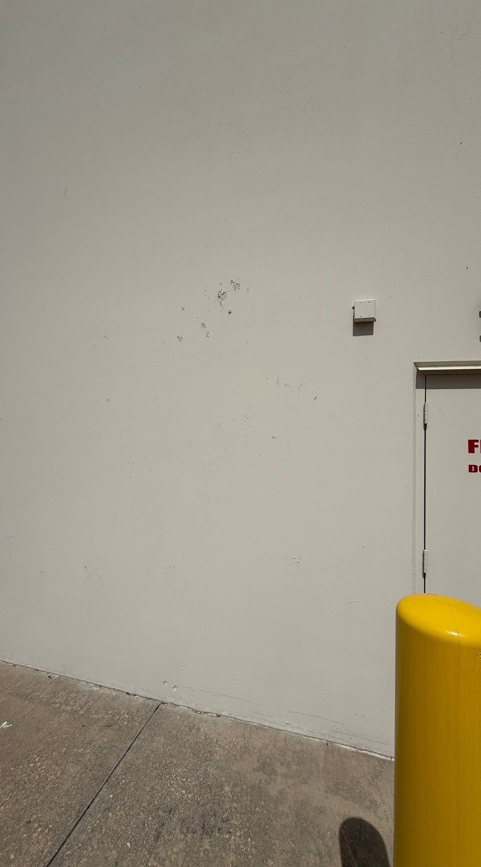 Exterior wall near a fire exit door of a commercial building on Highway 79 in Hutto, TX ahead of exterior painting by Hill Country Painting
