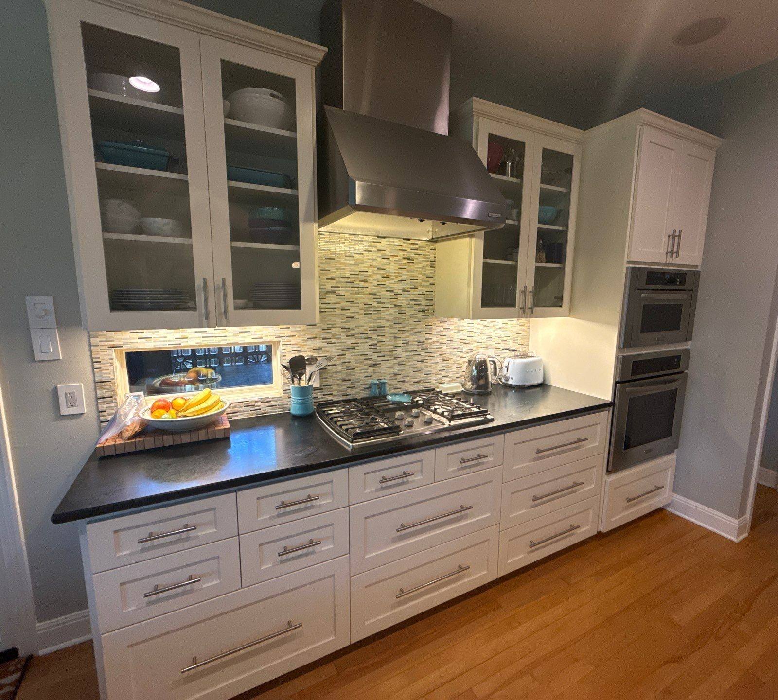 Wide view of kitchen cabinets, drawers, and stovetop ahead of painting